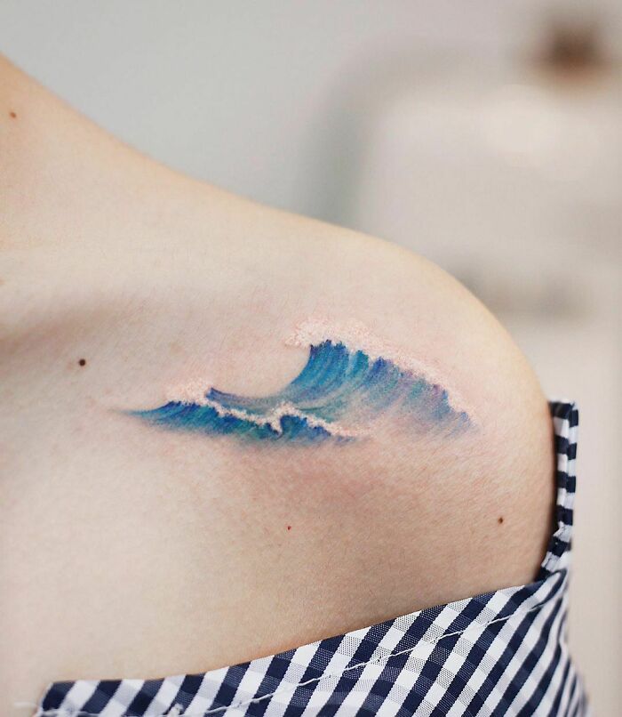 Color tattoo of an ocean wave on a shoulder, showcasing fine art details and vibrant shades.