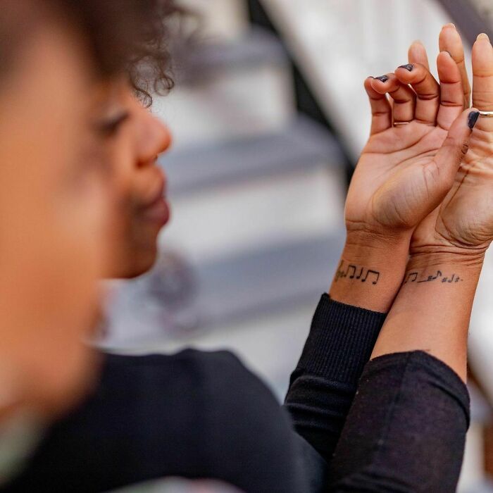 Person showing music note wrist tattoos, close-up, stylish accessory.