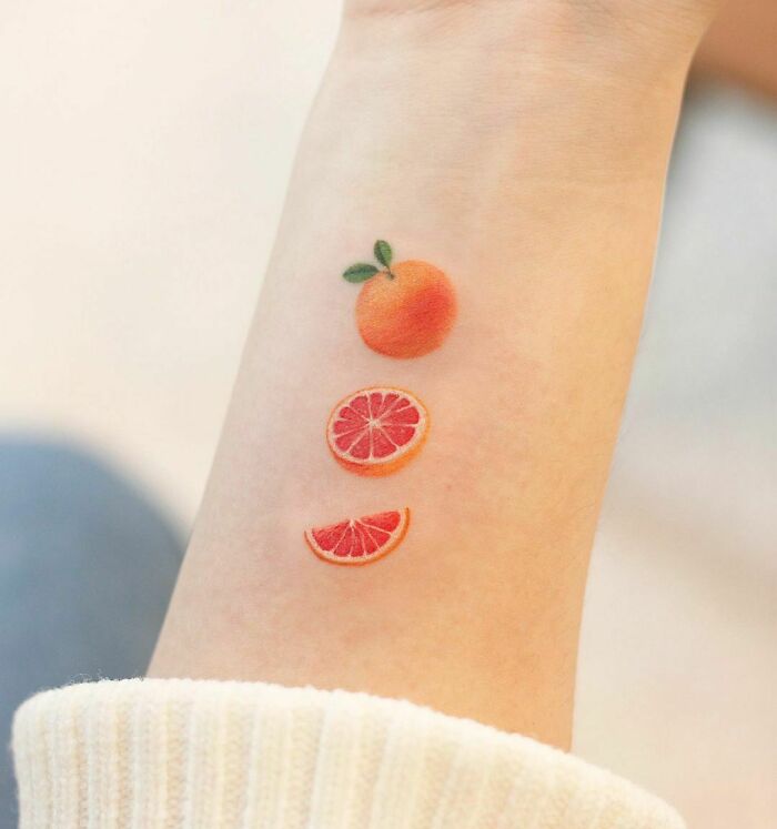 Color tattoo of an orange and slices on an arm, showcasing museum-quality art.