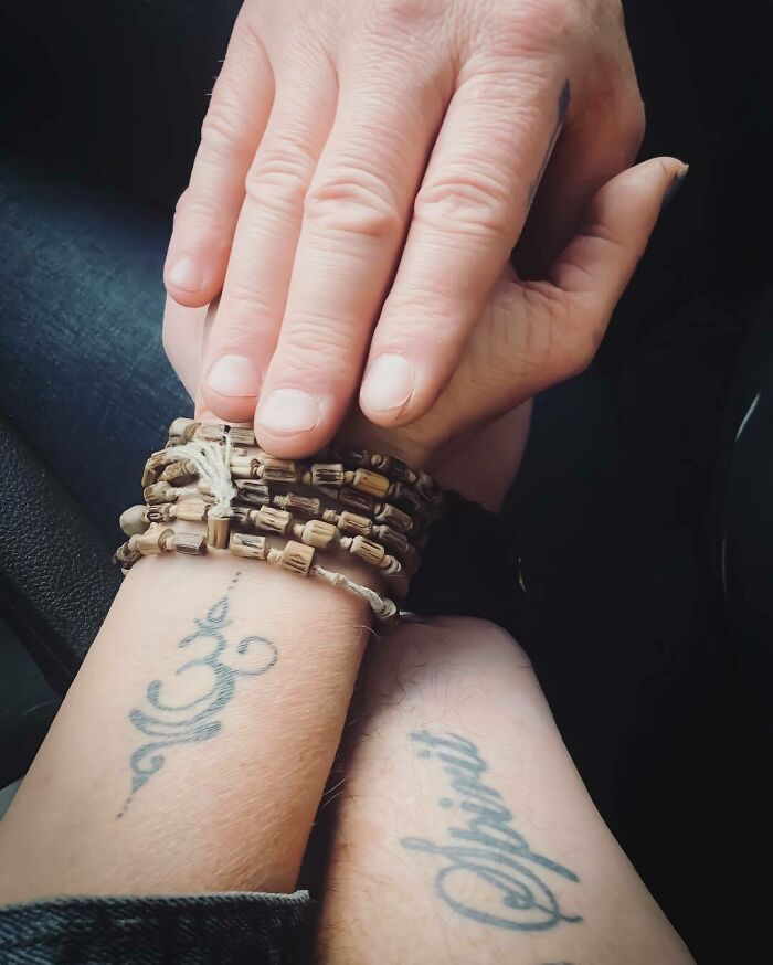 Wrist tattoos featuring cursive script and symbols on two wrists with bead bracelets.