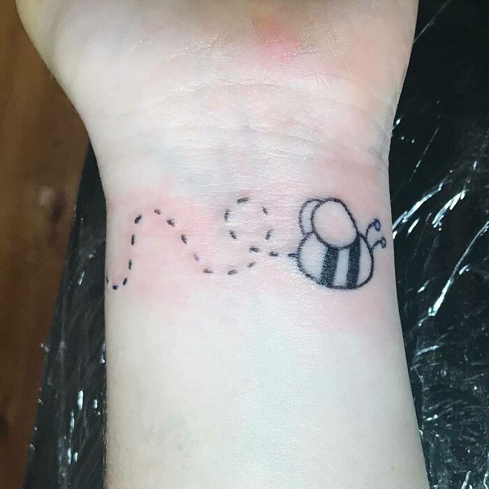 Wrist tattoo featuring a small bee with a dotted flight path.