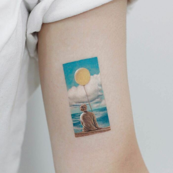 Color tattoo by Saegeem featuring a seated figure with a balloon against a beach and sky backdrop.