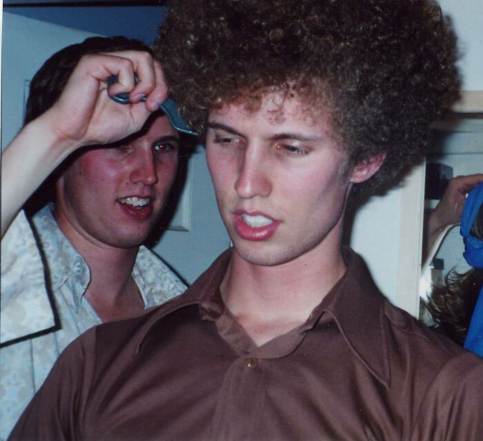Two celebrity twins at a casual indoor event, one with a large afro hairstyle, showcasing unique twin personalities.