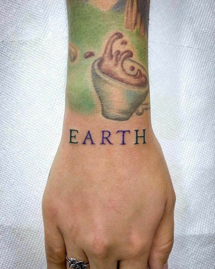 Wrist tattoo featuring the word "Earth" with abstract swirls and earthy colors.