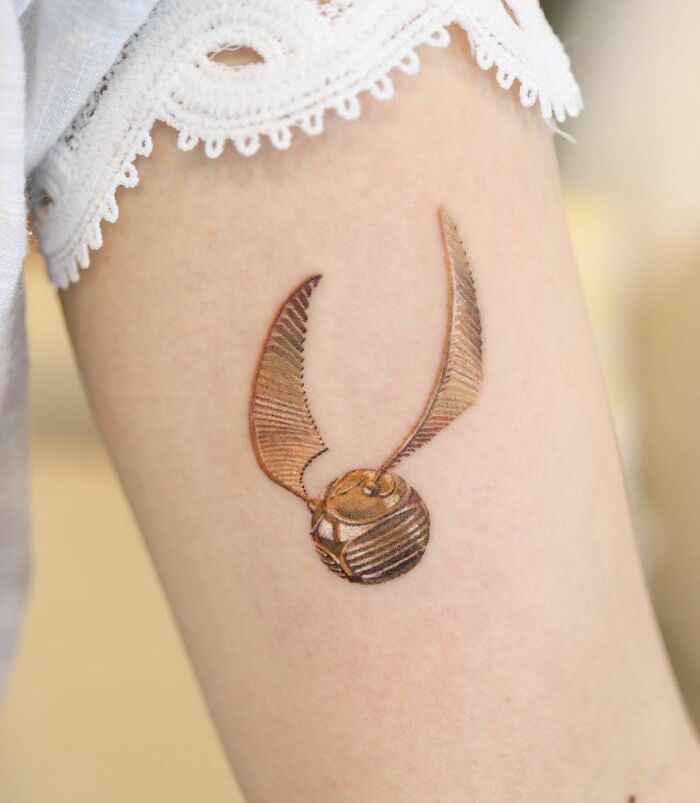 Color tattoo of a detailed golden snitch on an arm, showcasing exceptional artistic design by Saegeem.