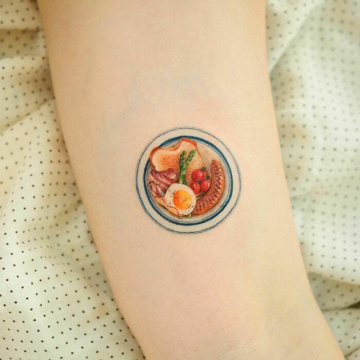 Color tattoo of a detailed breakfast plate on skin, showcasing exceptional artistry by Saegeem.
