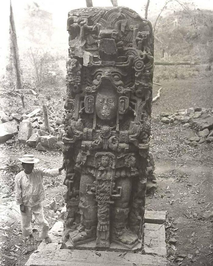 Man standing next to a large ancient carved stone statue in a forest, an important historical photo capturing archaeology.