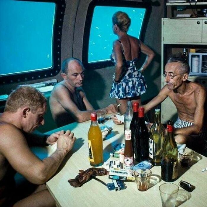 Men in swimwear inside a submarine dining area with bottles on the table, an important historical photo perspective.