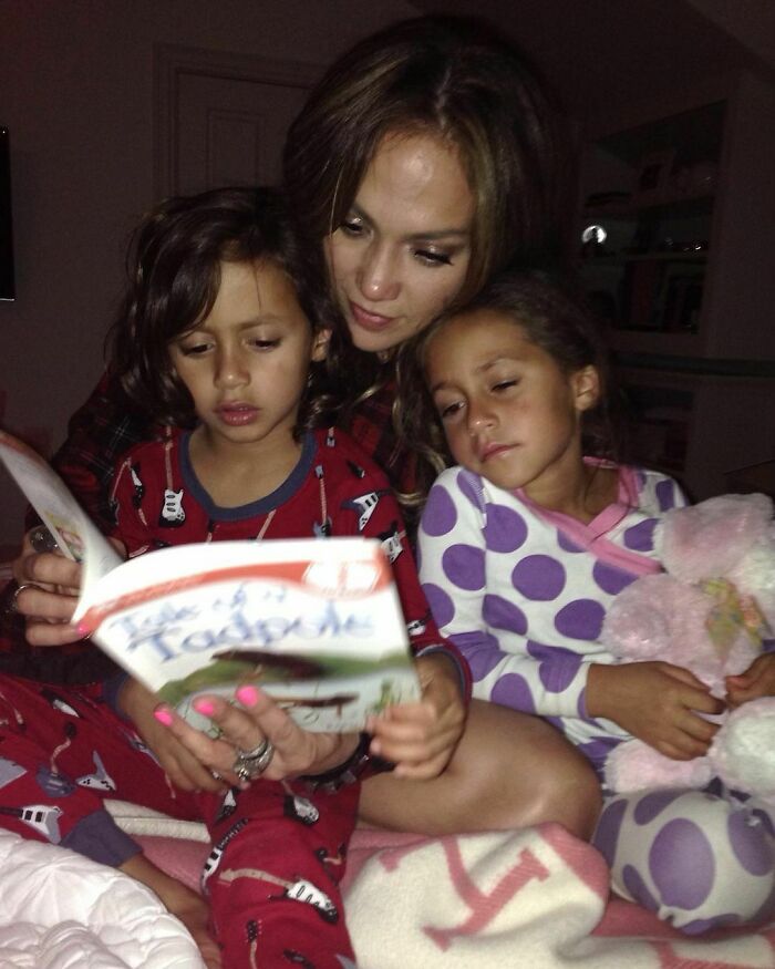 Woman reading a bedtime story to two young children in pajamas, highlighting celebrity twins bonding moments.