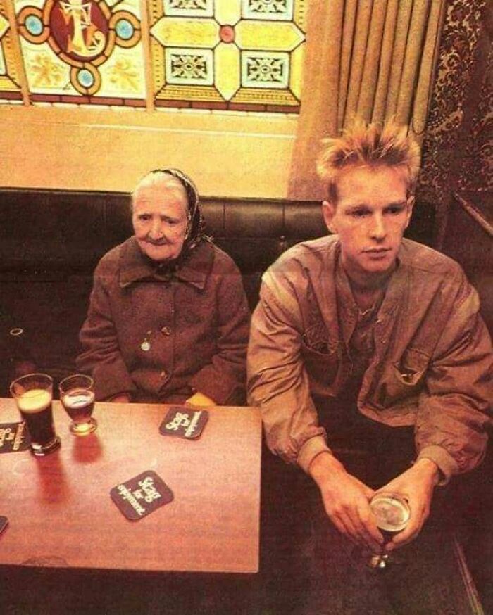 An important historical photo showing two strangers sitting silently in a pub with contrasting expressions and styles.