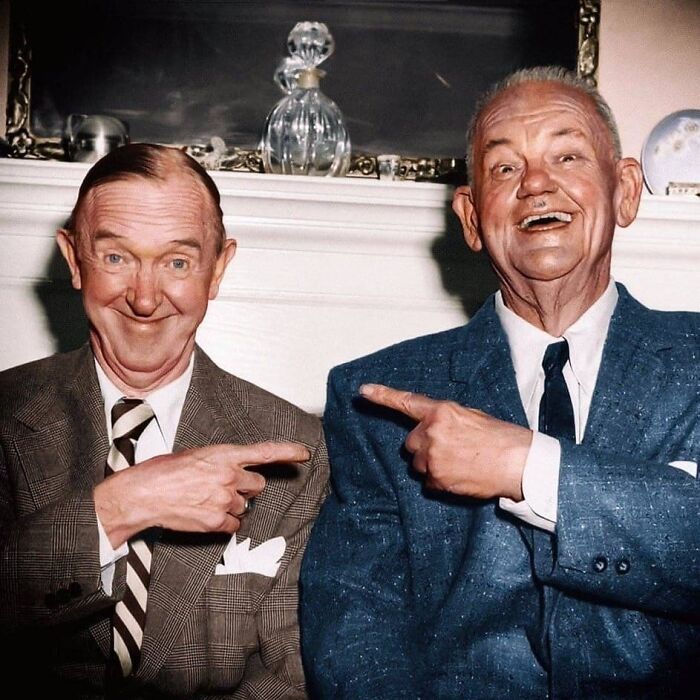 Two elderly men smiling and pointing at each other in a vintage setting, an important historical photo showcasing a unique moment.