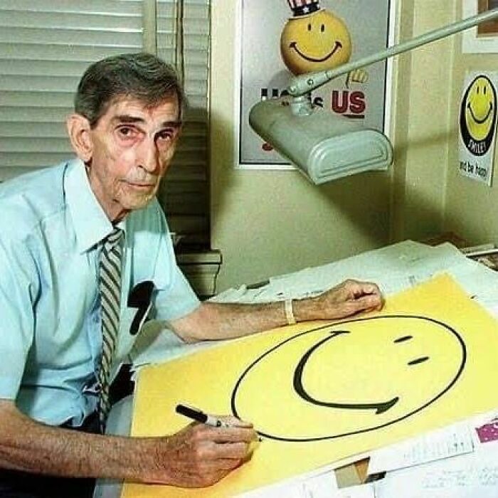 Older man drawing a large smiley face at a desk, an iconic image in important historical photos.