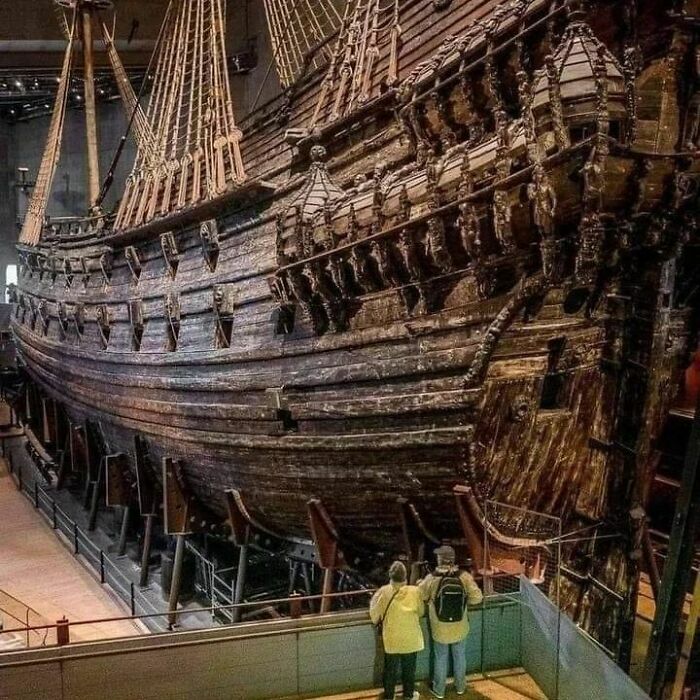 Large historical wooden ship displayed in a museum with visitors observing details in this important historical photo.