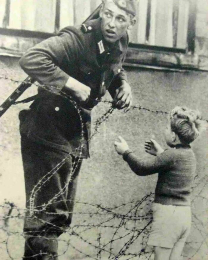 Soldier helping child cross barbed wire fence in a powerful important historical photo showing human compassion.