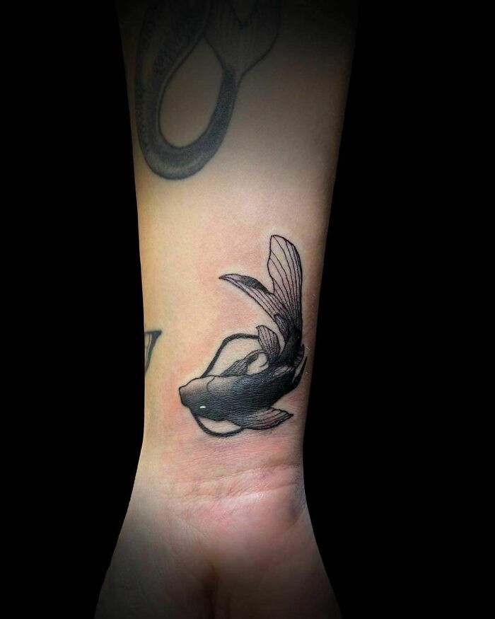 Koi fish wrist tattoo in black ink, showcasing elegant details and making a statement.