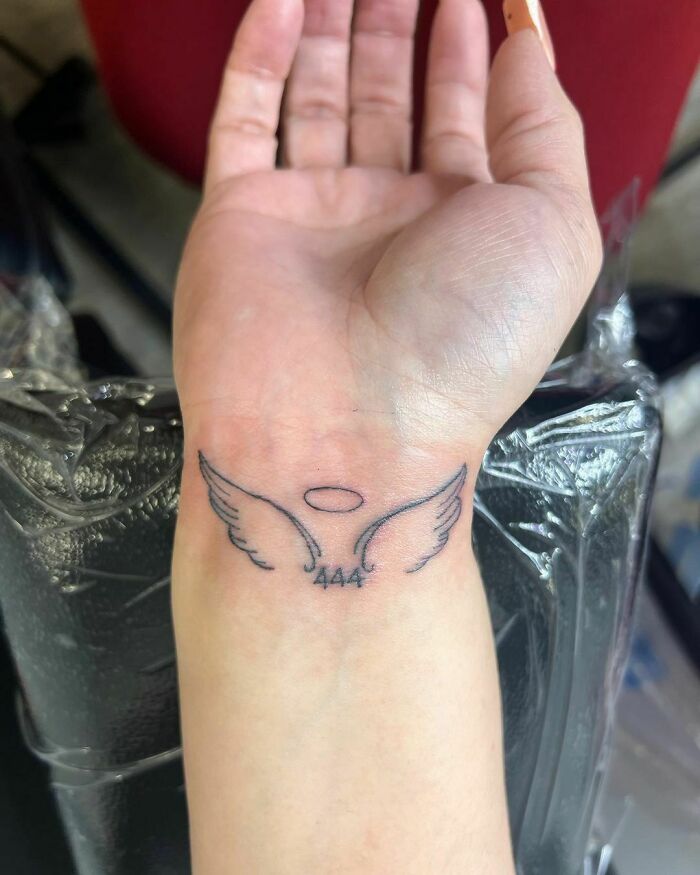 Angel wings wrist tattoo with halo and the number 444, symbolizing protection and guidance.