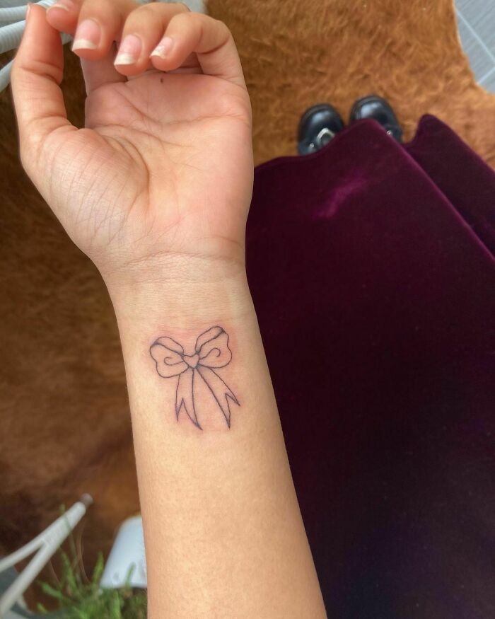 Close-up of a bow design wrist tattoo on a person's arm, showcasing trendy and timeless tattoo ideas.