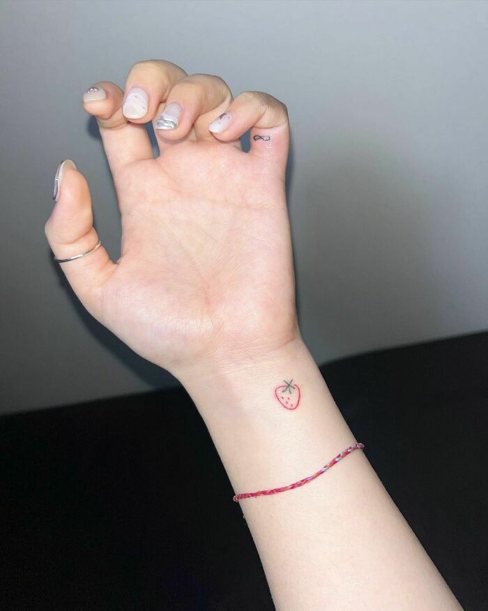 Small heart wrist tattoo design featuring a minimalist strawberry on a person’s arm.