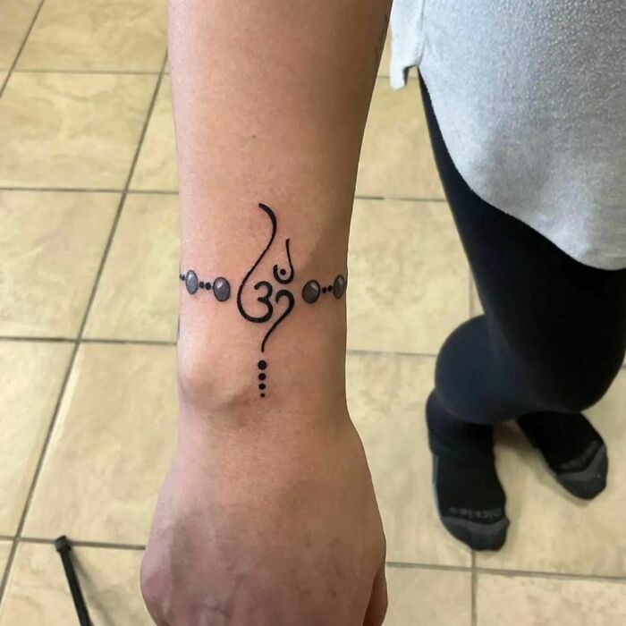 Ornate wrist tattoo featuring an Om symbol with decorative patterns, a timeless accessory.