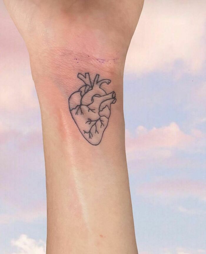 Detailed heart wrist tattoo design against a soft sky backdrop.