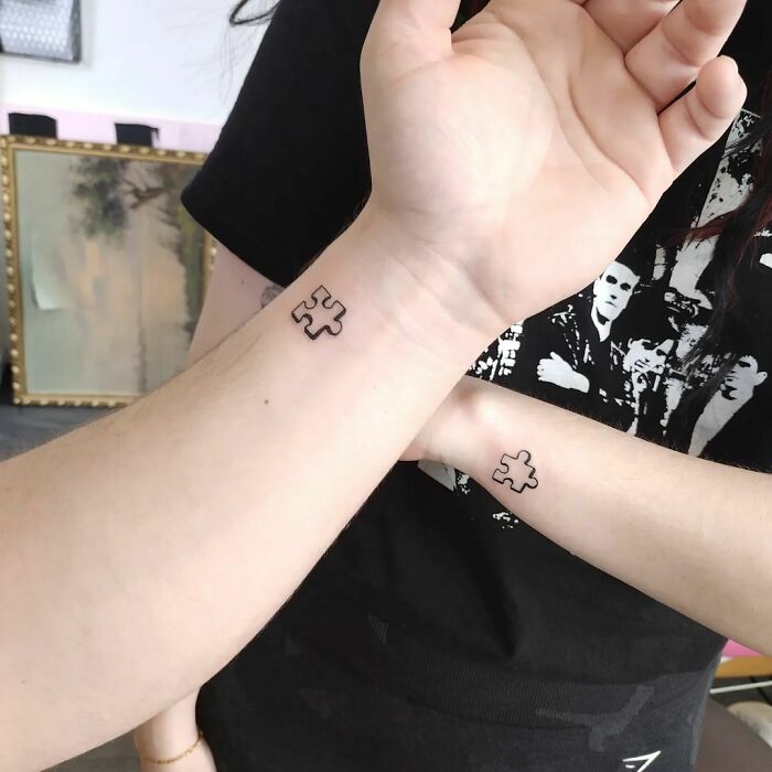 Minimalist wrist tattoos featuring puzzle piece designs on two people.