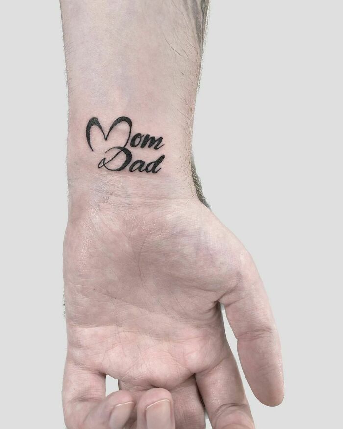 "Wrist tattoo with 'Mom Dad' in elegant script on a person's forearm."
