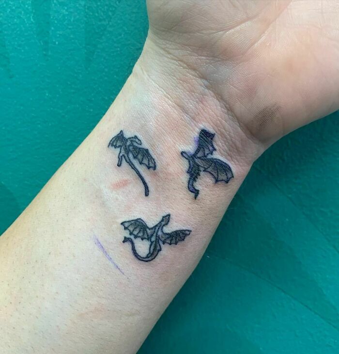 Dragon wrist tattoo design with three small, black dragons on the skin against a green background.
