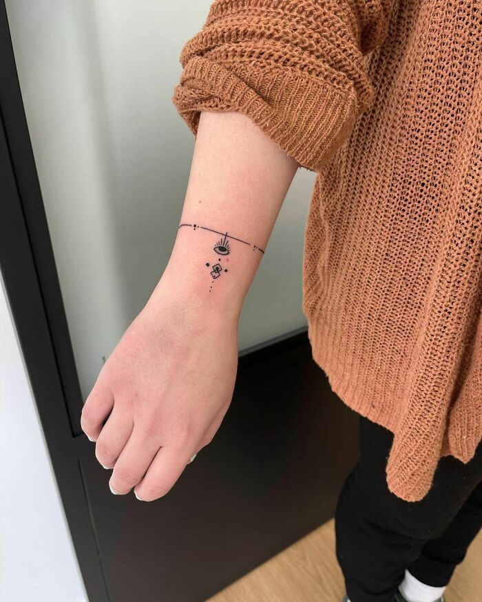 Minimal wrist tattoo design on person wearing a brown sweater.