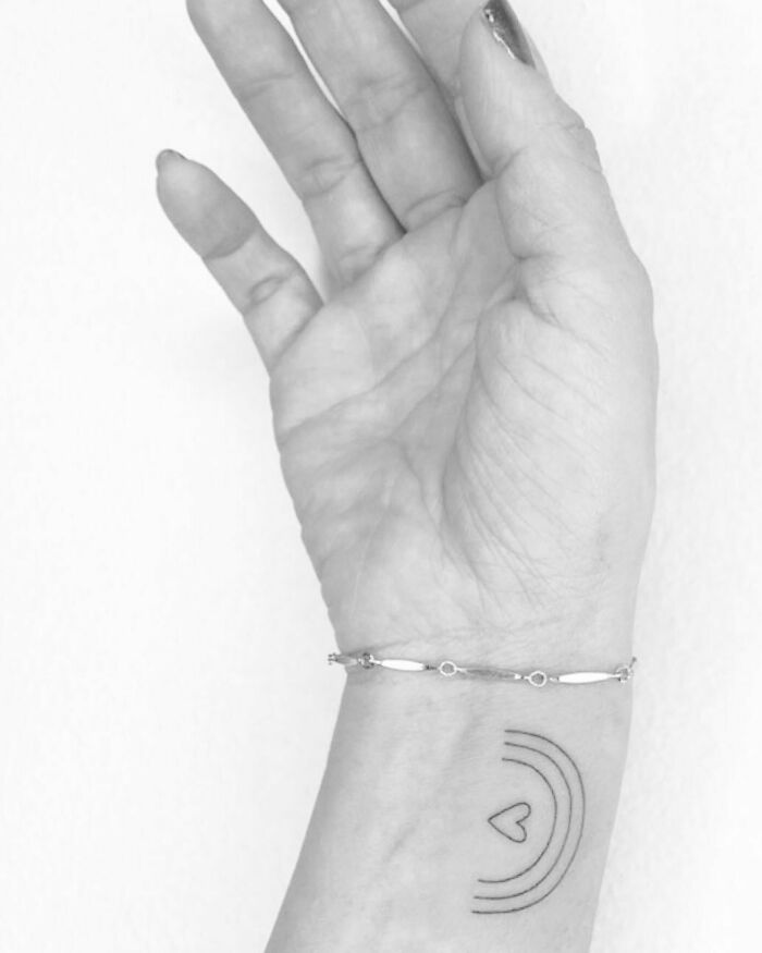 Minimalist wrist tattoo featuring concentric lines and a small heart design.