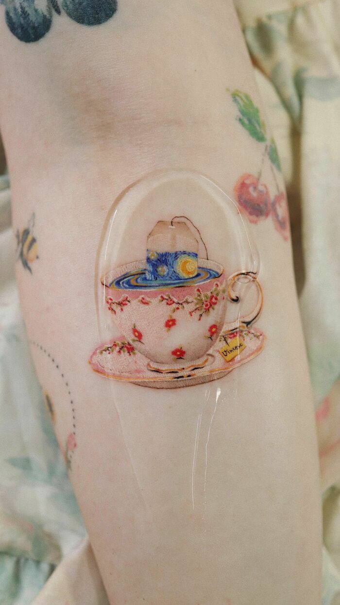 Color tattoo of a floral teacup with Van Gogh's Starry Night theme on arm.