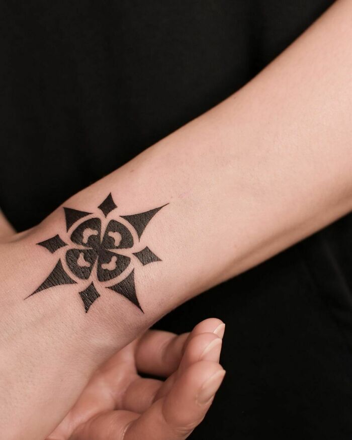 Geometric black wrist tattoo design on forearm against a black background.
