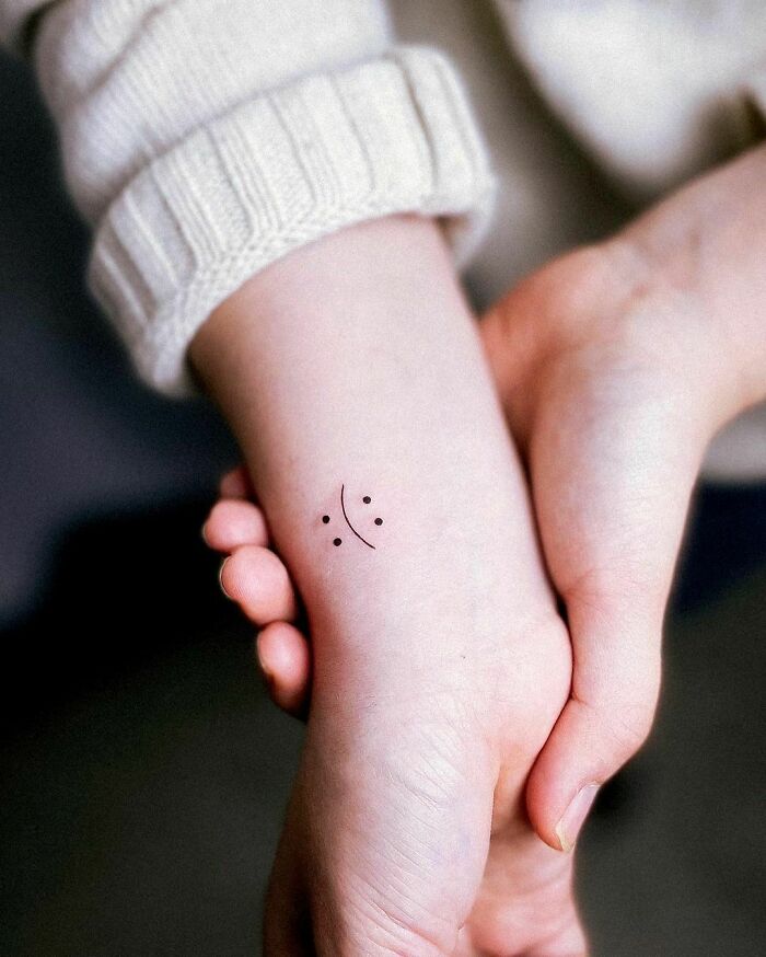 Minimalist wrist tattoo design with a small smiley face.