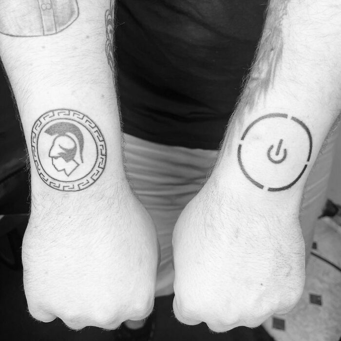 Two wrist tattoos: one of a Greek helmet and the other a power button symbol.