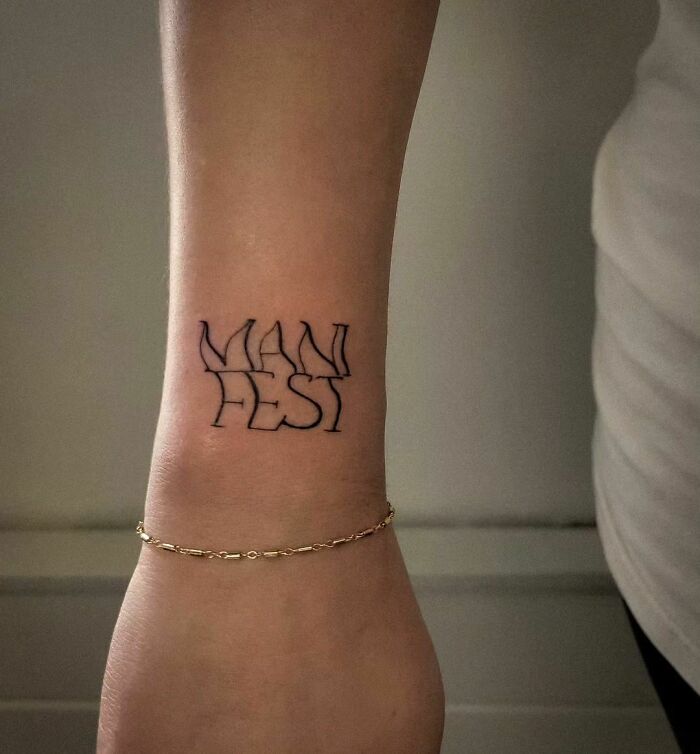 "Wrist tattoo with the word 'MANIFEST' in bold, showcasing a popular design style."