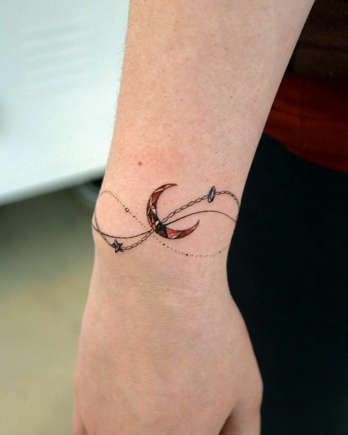 Delicate crescent moon and star wrist tattoo with fine line detailing.