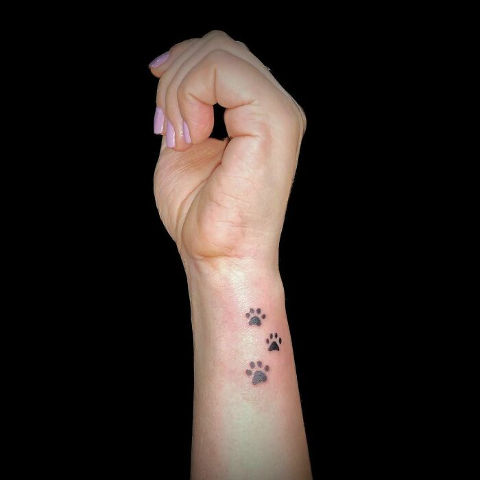Wrist tattoo with small paw prints on a raised wrist, simple and stylish design.