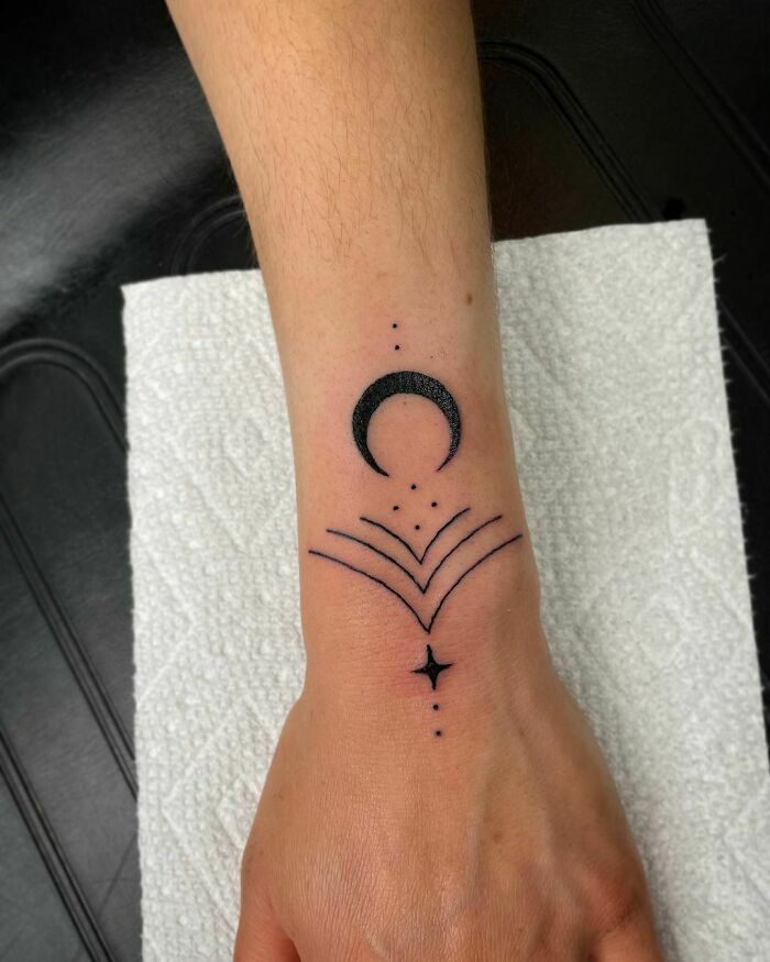 Minimalist wrist tattoo featuring a crescent moon and geometric designs, showcasing stylish body art.