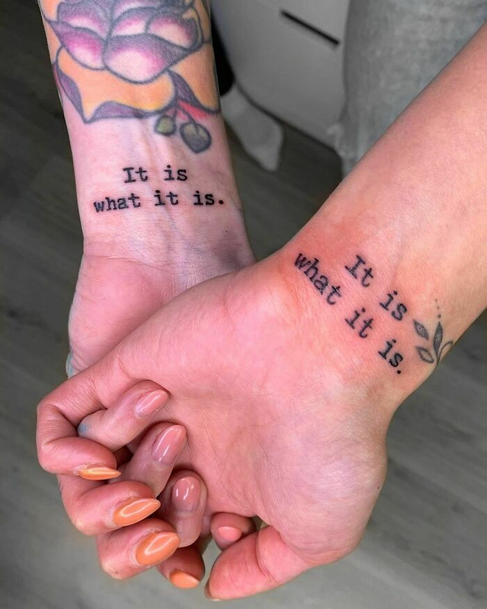 Two wrists with matching "It is what it is" tattoos, held together, showcasing a meaningful wrist tattoo idea.