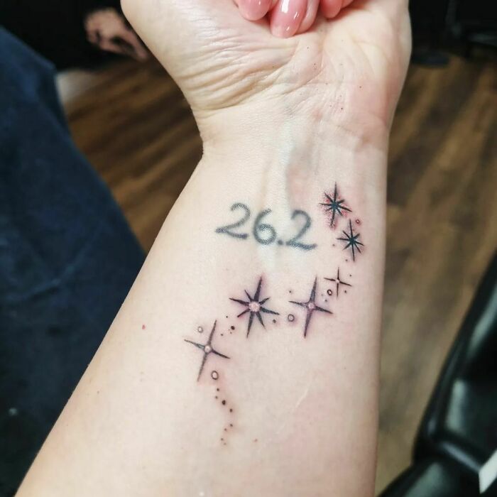 Wrist tattoo with "26.2" and star designs, symbolizing marathon achievement.