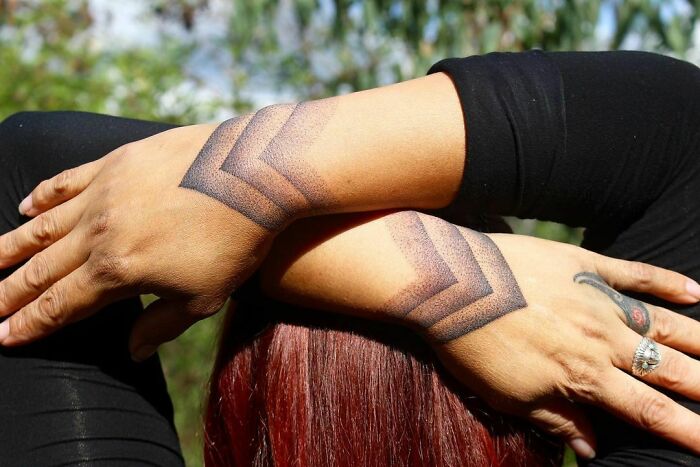 Geometric wrist tattoo with bold chevron patterns on crossed arms.