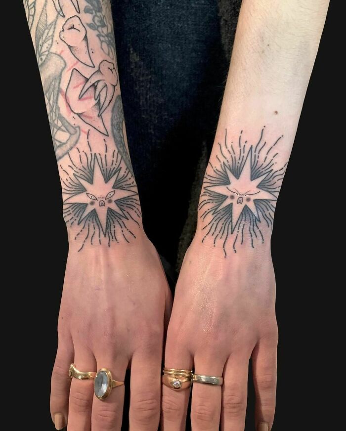 Star wrist tattoos with line details on both forearms, adorned with rings.