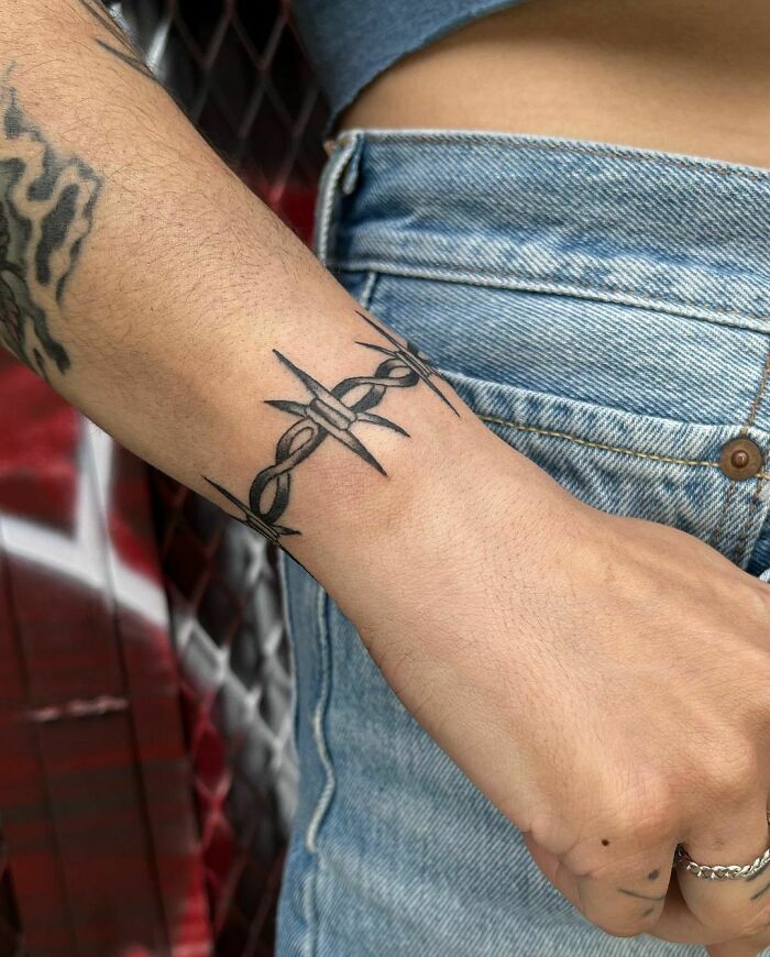 Barbed wire wrist tattoo on arm, styled as a timeless accessory.