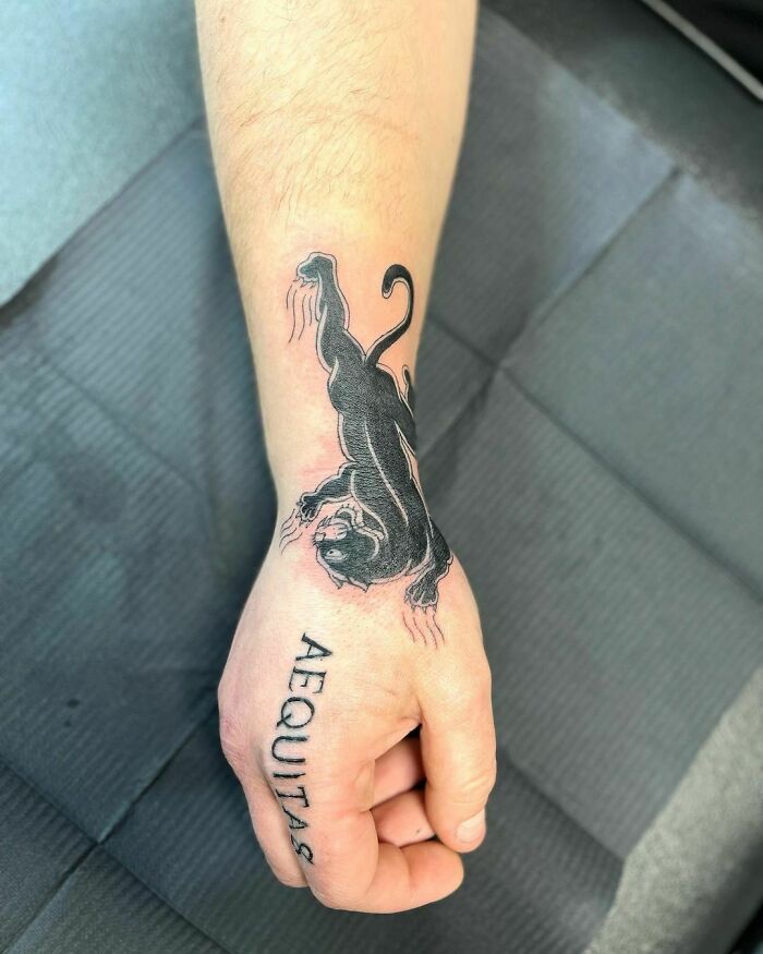 Black panther wrist tattoo with "AEQUITAS" text, showcasing stylish and timeless tattoo ideas.