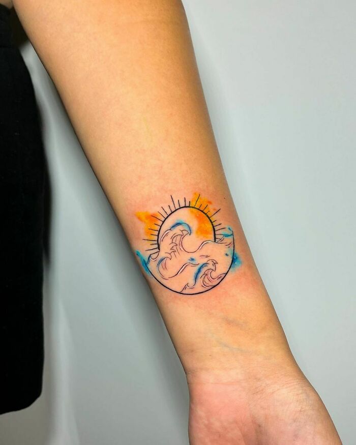 Colorful wave wrist tattoo with sun design, featuring orange and blue tones.