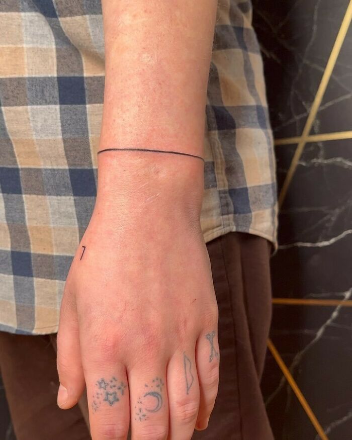 Simple black line wrist tattoo design with small, celestial tattoos on fingers.