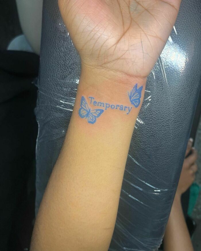 Wrist tattoo with blue butterflies and the word "Temporary" in elegant script.