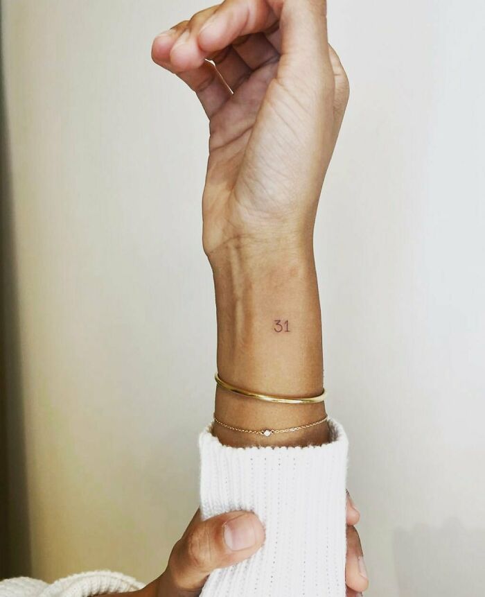 Minimalist wrist tattoo with number 31, adorned with gold bracelets.