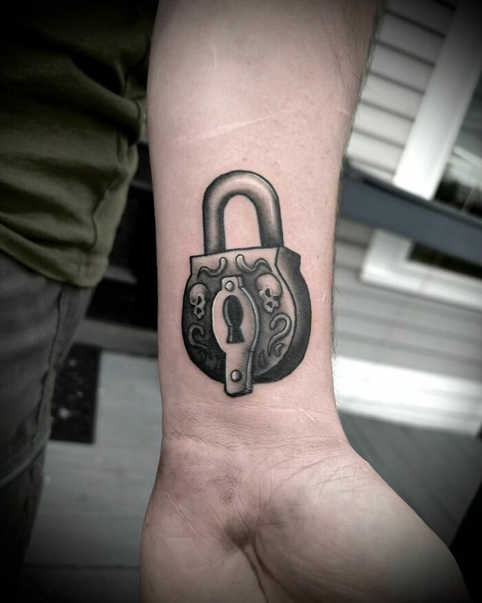 Wrist tattoo of a lock with skull designs, showcasing bold statement.