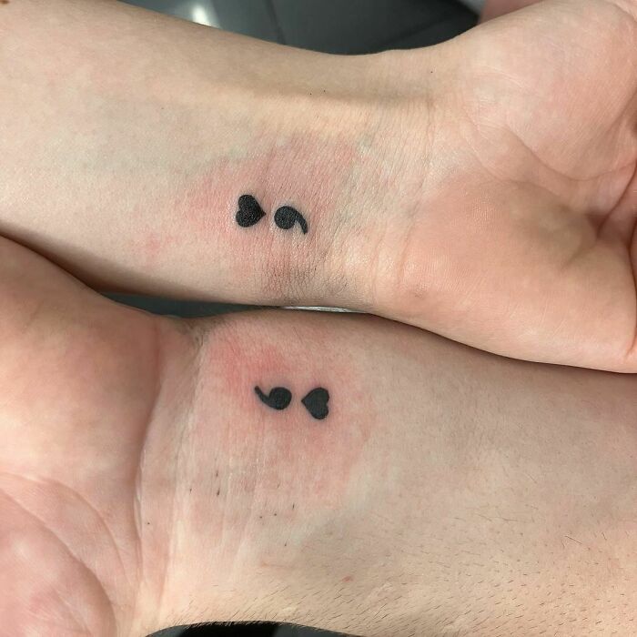 Matching semicolon and heart wrist tattoos on two wrists.