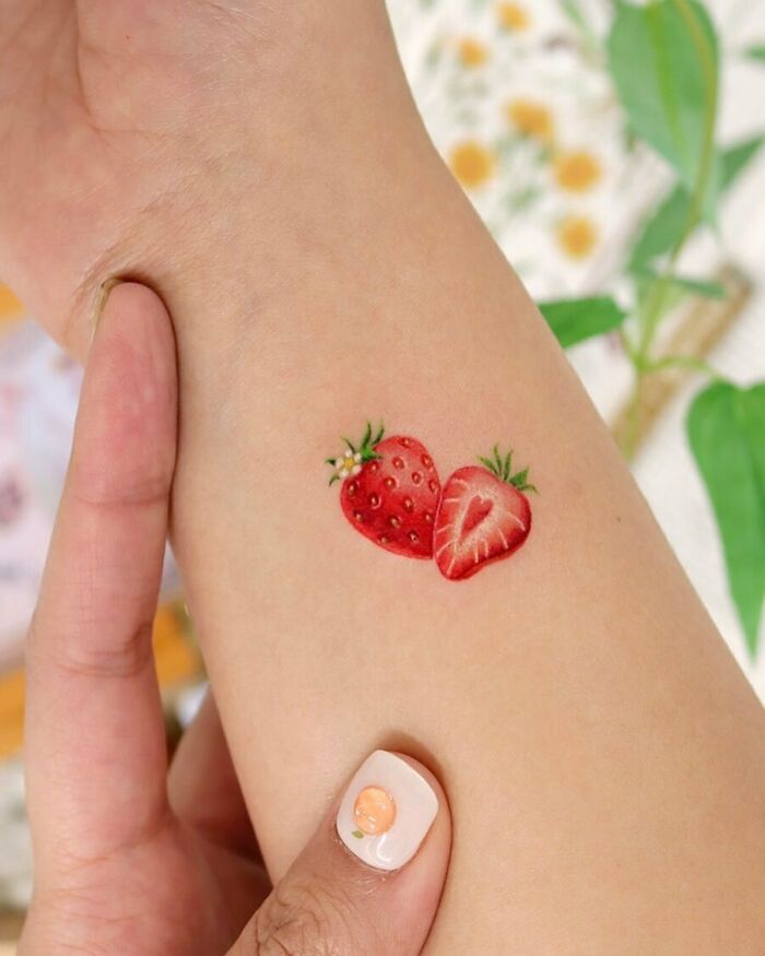 Strawberry wrist tattoo design on a person's arm, showcasing vibrant reds and greens.